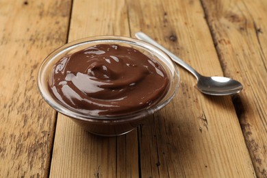 Photo of Delicious chocolate mousse in glass bowl and spoon on wooden table, closeup