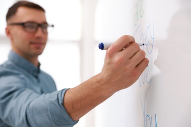 Photo of English teacher writing on whiteboard during lesson in classroom, selective focus