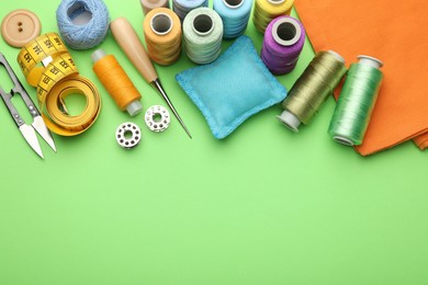 Photo of Different sewing supplies on green background, flat lay. Space for text