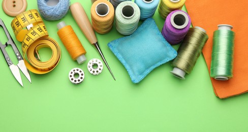 Photo of Different sewing supplies on green background, flat lay. Space for text