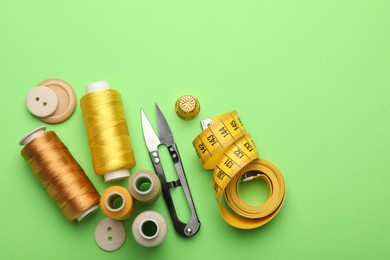 Photo of Different sewing supplies on green background, flat lay. Space for text