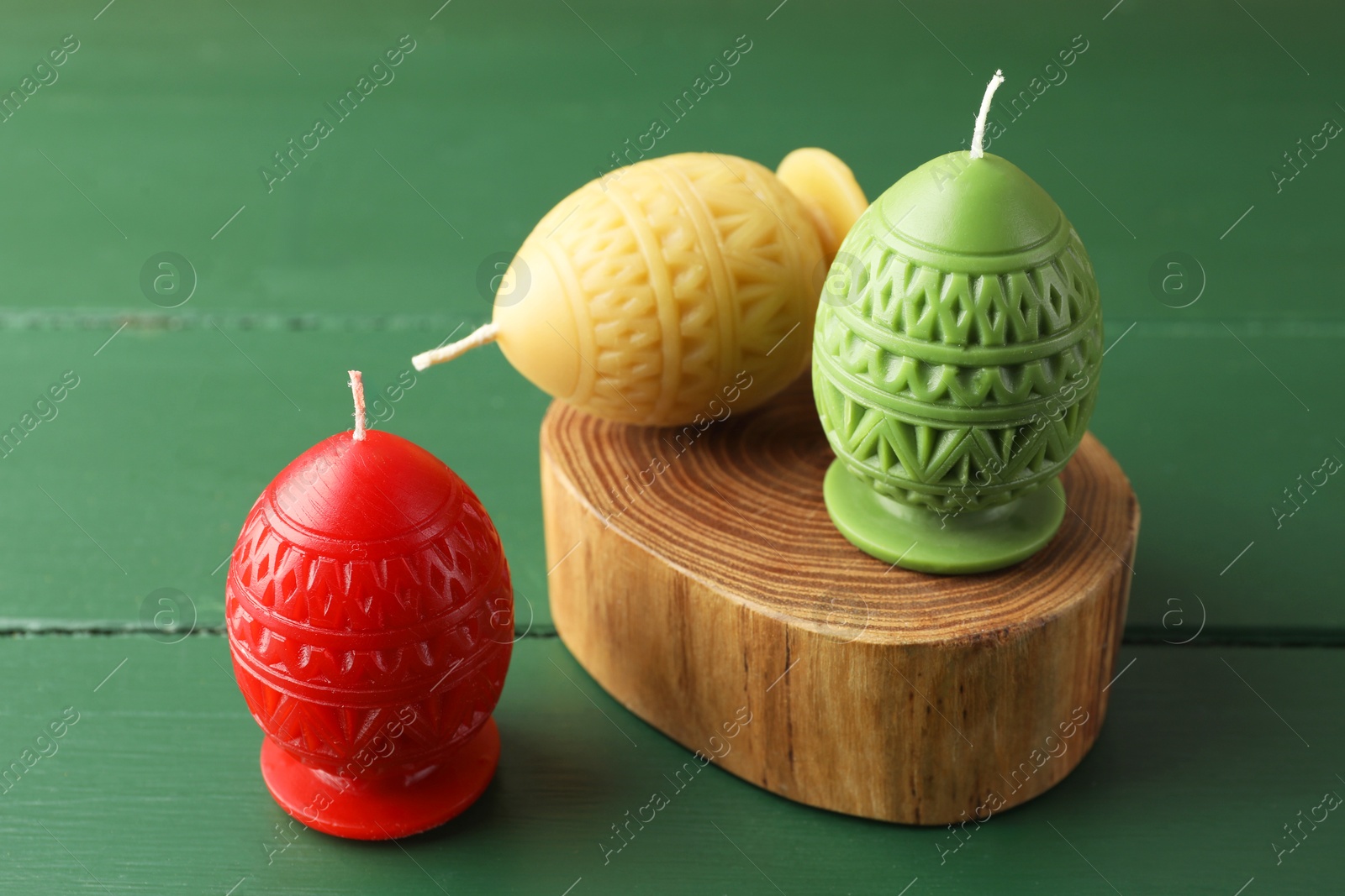 Photo of Colorful egg-shaped candles on green wooden table, closeup. Easter decor