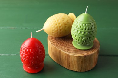 Photo of Colorful egg-shaped candles on green wooden table, closeup. Easter decor