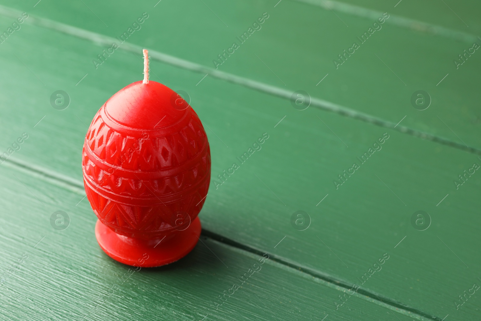 Photo of Red egg-shaped candle on green wooden table, space for text. Easter decor