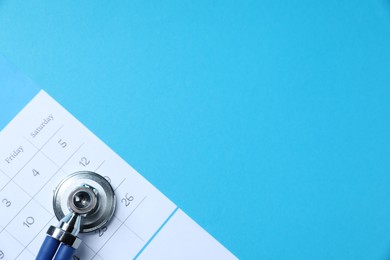 Photo of Stethoscope and calendar on light blue background, top view. Space for text