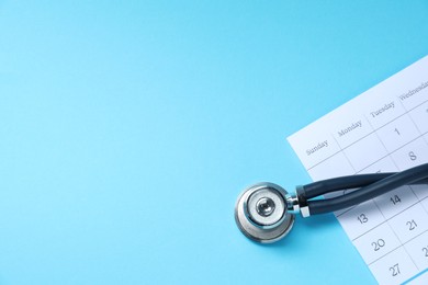 Photo of Stethoscope and calendar on light blue background, top view. Space for text