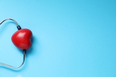 Photo of Stethoscope and red decorative heart on light blue background, top view. Space for text