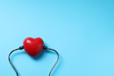 Photo of Stethoscope and red decorative heart on light blue background, top view. Space for text