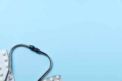 Stethoscope and pills on light blue background, flat lay. Space for text
