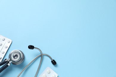 Photo of Stethoscope and pills on light blue background, flat lay. Space for text