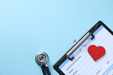 Photo of Stethoscope, medical card form and red decorative heart on light blue background, flat lay. Space for text