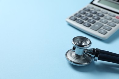 Photo of Stethoscope and calculator on light blue background, closeup. Space for text