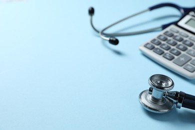 Photo of Stethoscope and calculator on light blue background, closeup. Space for text