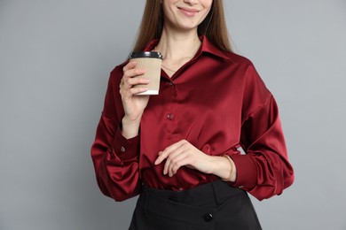 Photo of Beautiful woman in stylish outfit with cup of coffee on grey background, closeup