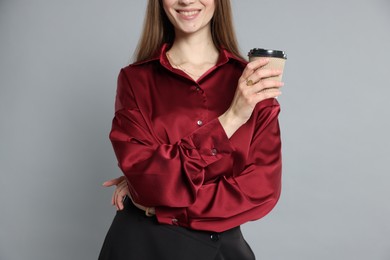 Photo of Beautiful woman in stylish outfit with cup of coffee on grey background, closeup