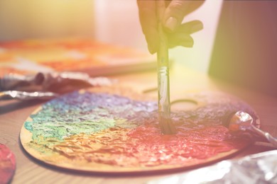 Image of Artist mixing paints with brush on palette in sunlit studio, closeup