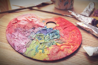 Image of Artist's palette with many mixed paints on wooden table, closeup