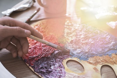 Image of Artist mixing paints with brush on palette in sunlit studio, closeup