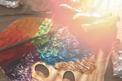 Image of Palette with brush and mixed paints in sunlit artist's studio, closeup