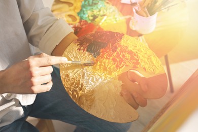 Image of Artist mixing paints with brush on palette in sunlit studio, closeup