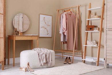 Photo of Stylish ottoman, console table and clothing rack in dressing room. Interior design