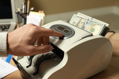 Photo of Man using banknote counter at wooden table indoors, closeup