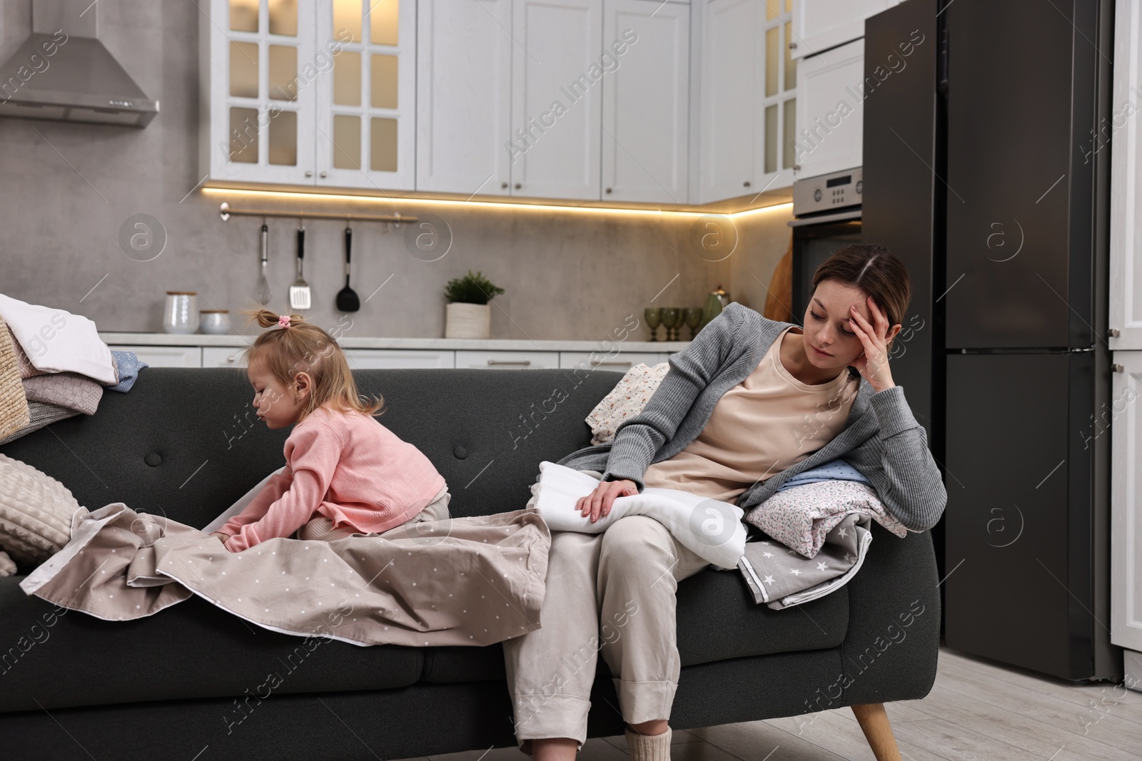 Photo of Housewife with her little daughter folding laundry on sofa at home