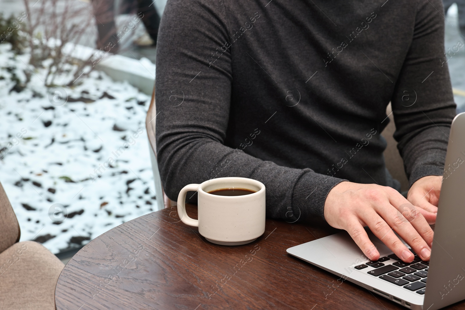 Photo of Businessman typing on laptop during coffee break at wooden table in cafe, closeup