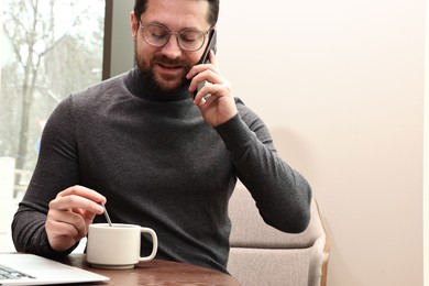 Photo of Businessman talking by smartphone during coffee break in cafe. Space for text