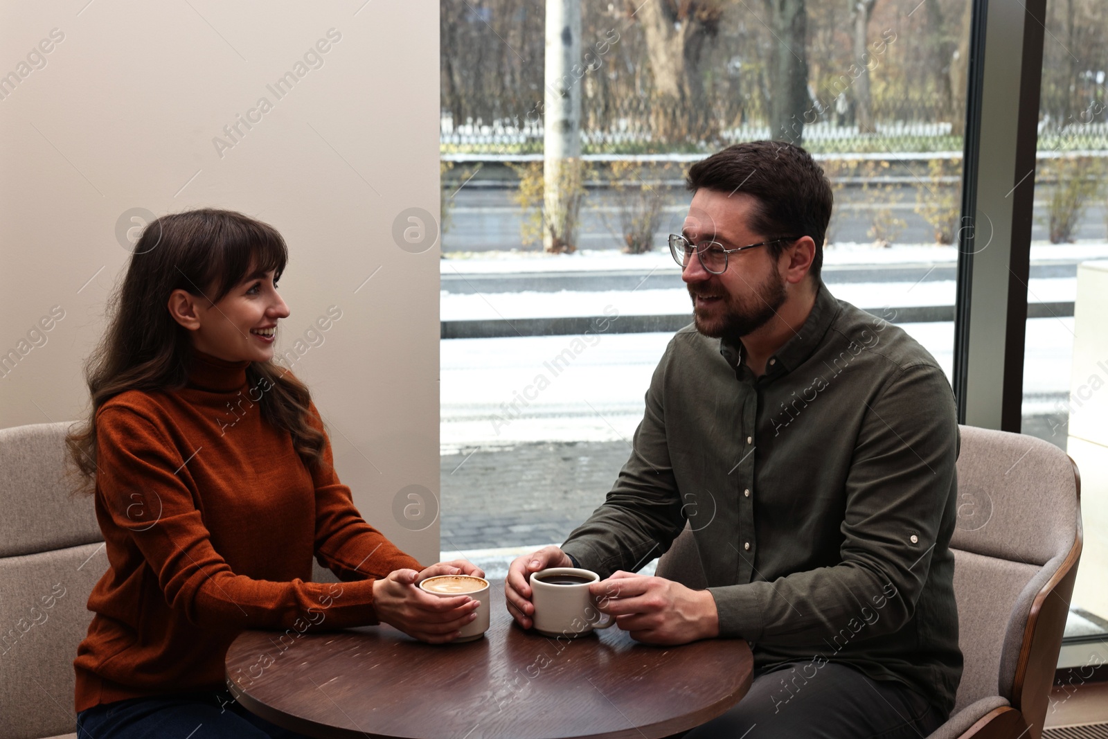 Photo of Happy colleagues talking during coffee break at wooden table in cafe