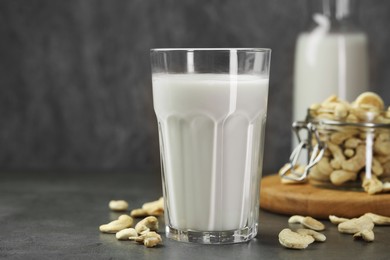 Photo of Fresh cashew milk in glass and nuts on grey table, closeup. Space for text