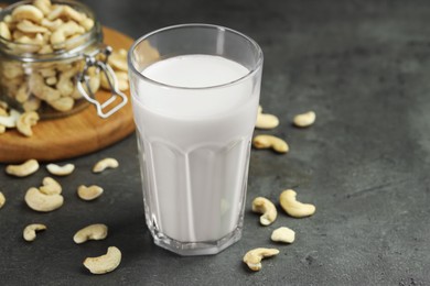 Photo of Fresh cashew milk in glass and nuts on grey table, closeup