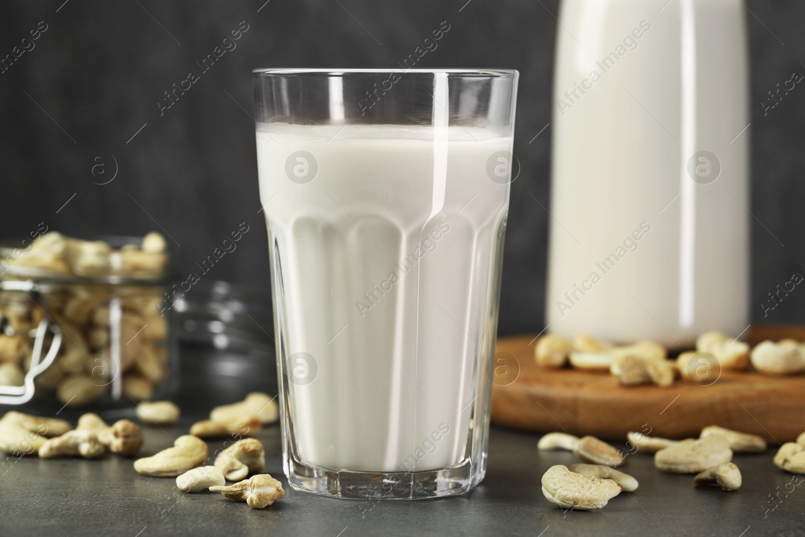 Photo of Fresh cashew milk in glass and nuts on grey table, closeup