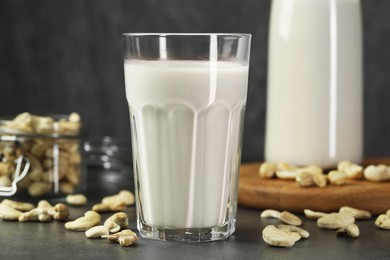 Photo of Fresh cashew milk in glass and nuts on grey table, closeup