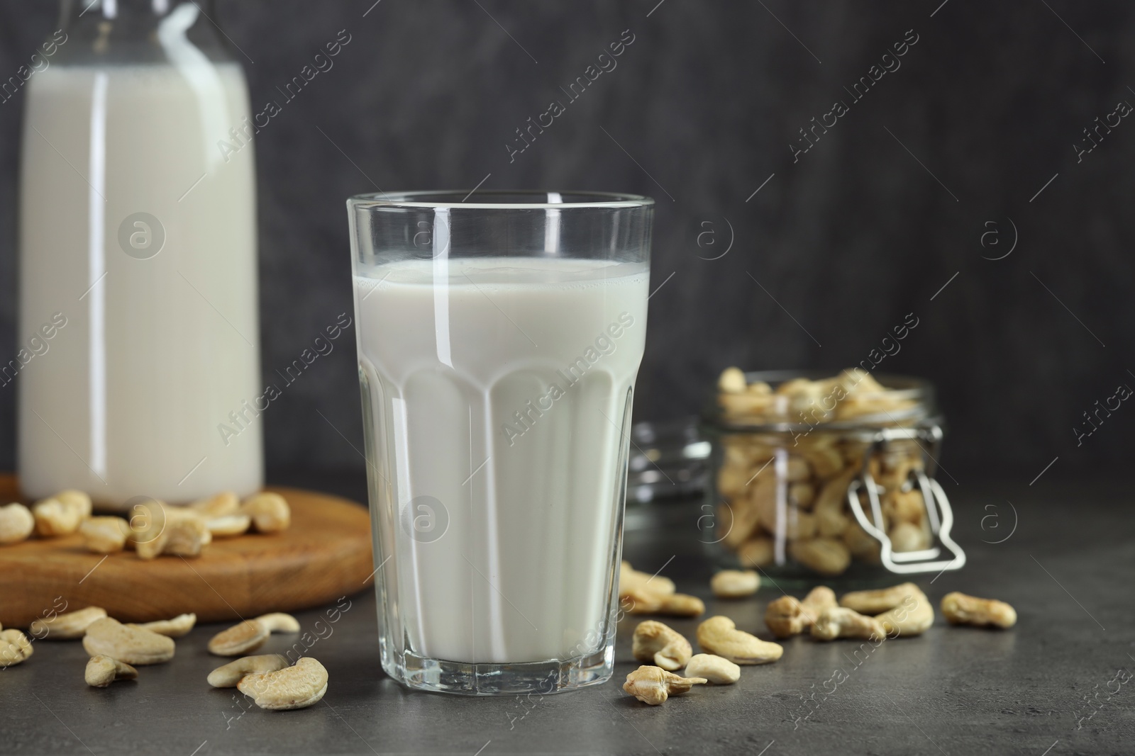 Photo of Fresh cashew milk in glass and nuts on grey table