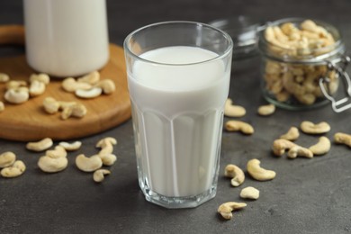 Fresh cashew milk in glass and nuts on grey table, closeup