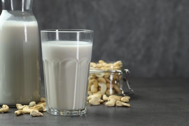 Fresh cashew milk in glass and nuts on grey table, space for text