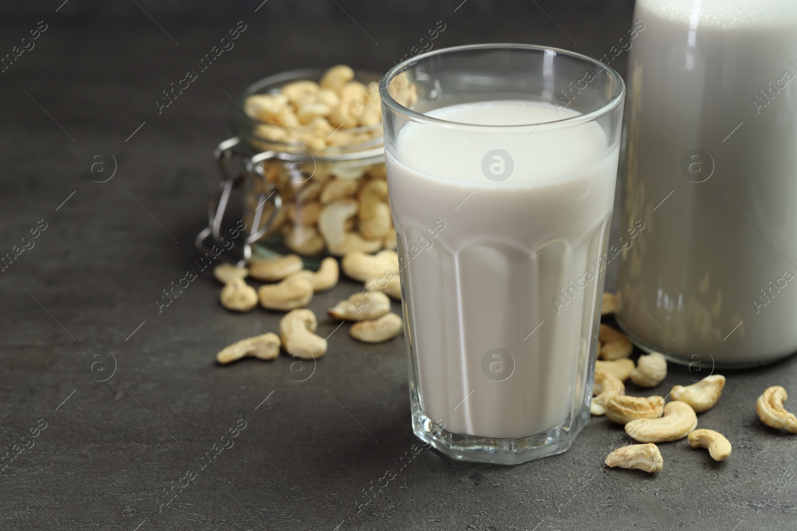 Photo of Fresh cashew milk in glass and nuts on grey table, closeup. Space for text