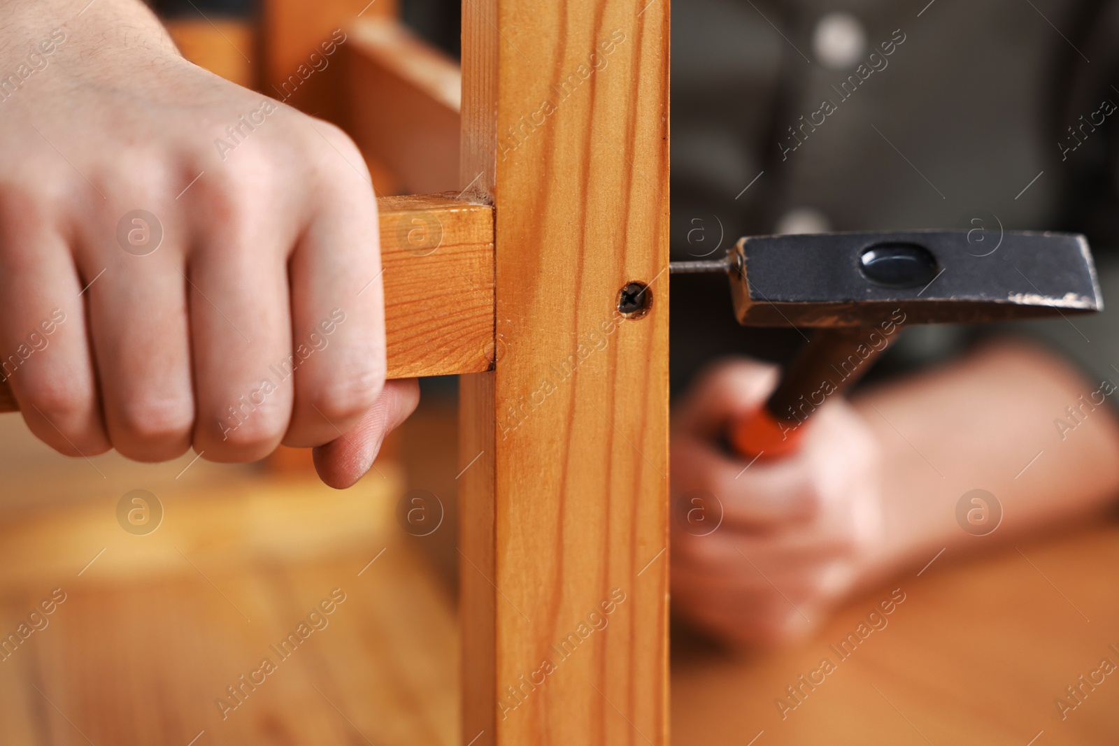 Photo of Man repairing wooden stool with nail and hammer at home, closeup