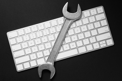 Photo of Technical support concept. Wrench and keyboard on black background, top view