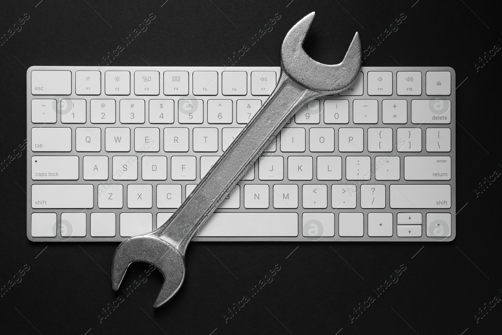 Photo of Technical support concept. Wrench and keyboard on black background, top view