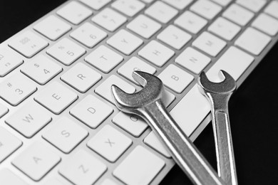 Photo of Technical support concept. Wrenches and keyboard on black background, closeup