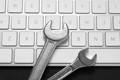 Photo of Technical support concept. Wrenches and keyboard on black background, top view