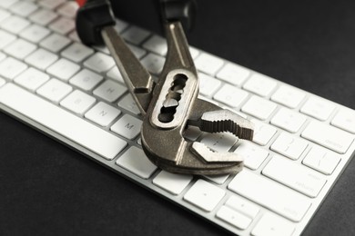 Photo of Technical support concept. Plumbing pliers and keyboard on black background, closeup