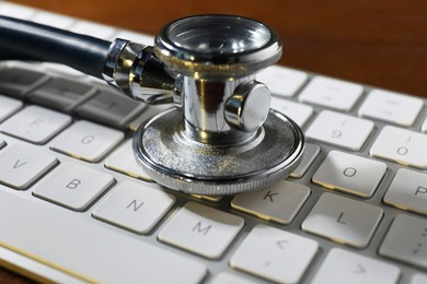 Photo of Technical support concept. Stethoscope and keyboard on wooden table, closeup