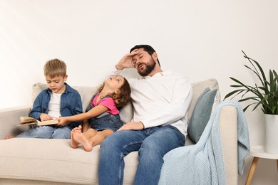 Photo of Overwhelmed father and his hyperactive children on sofa at home