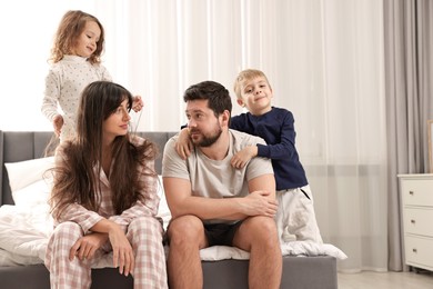 Photo of Playful children and their overwhelmed parents on bed at home