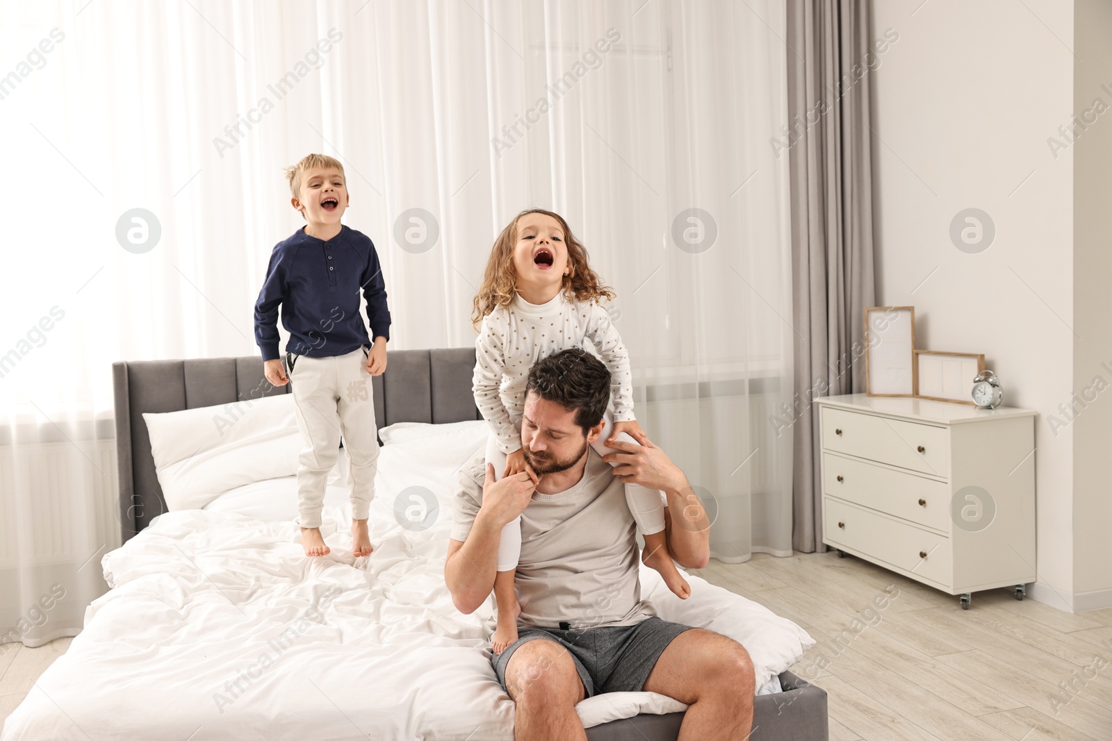 Photo of Overwhelmed father and his naughty children on bed at home