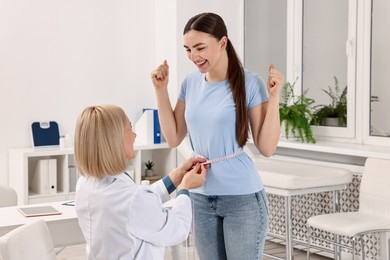 Photo of Happy woman lost weight. Nutritionist measuring patient's waist with tape in clinic