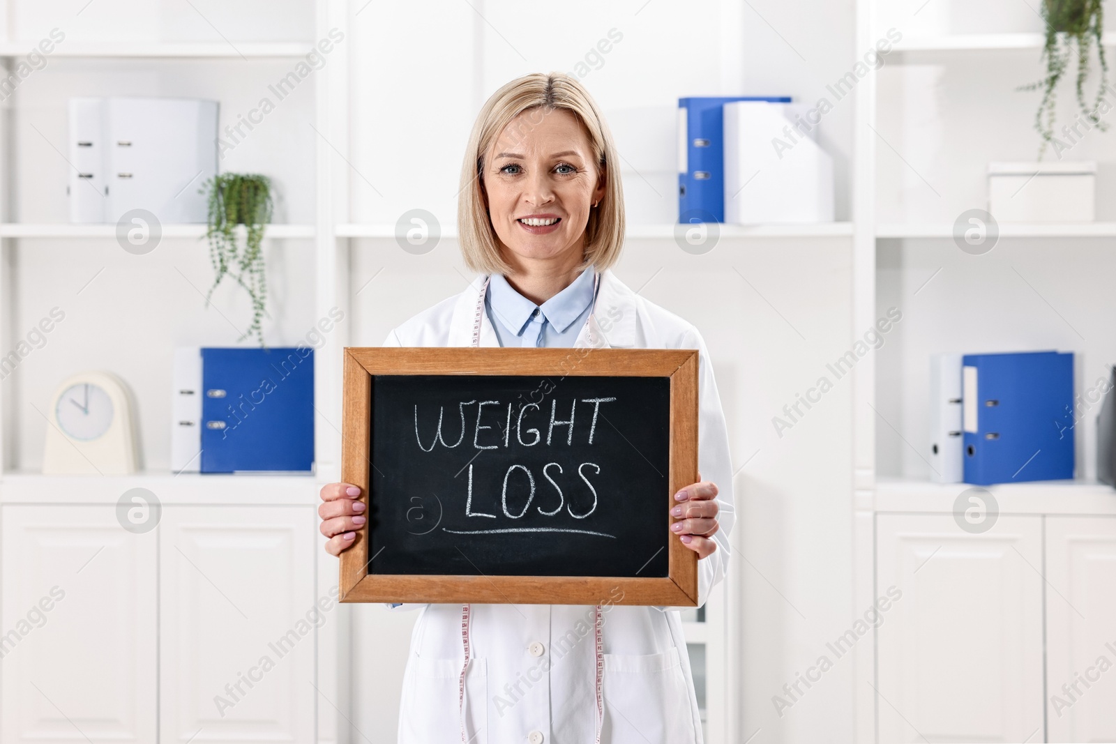 Photo of Happy nutritionist holding small blackboard with words Weight loss in clinic